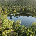 Scenic Lake View With Sunlight Through Trees Mountain Backdrop And Calm Water Reflections