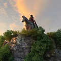 Ancient Warrior on Horseback Standing Atop Hilltop With Green Trees and Sunset Sky