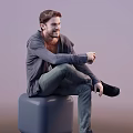 A Man Sitting On Gray Cube Wearing Gray Cardigan And Dark Pants With Beard