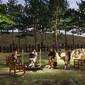 Wooded Camping Site With Campfire People Sitting Around And Natural Surroundings