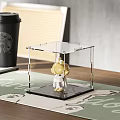 Cute Yellow Doll In Clear Transparent Display Case Placed On Table With Green Mat Background