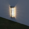 Modern Wall Sconce with Metal Frame and Glass Illuminating White Wall Above Green Grass