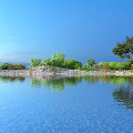 Peaceful Lakeside Natural Scenery With Clear Reflective Water Lush Green Trees Under Bright Blue Sky