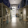 Simple Dormitory Room Interior With Bunk Beds Desks Chairs And Hanging Clothes