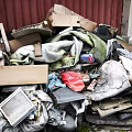 Waste Pile with Tire Wooden Board Fabric Old Electronics Cardboard Boxes and Red Brick Wall