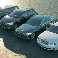 Different Luxury Cars Parked By Waterfront On Stone Pavement Under Sunlight