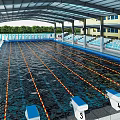 Covered Swimming Pool With Lane Lines Starting Blocks Spectator Seats And Surrounding Buildings