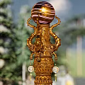 Golden Columnar Landscape Sculpture Surrounded by Pine Trees Blue Sky and Stone Steps