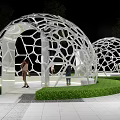 White Geodesic Pergola with Hollowed-out Geometric Patterns Surrounded by Green Lawn in Nighttime Illumination