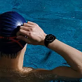 Person Wearing Waterproof Smartwatch Adjusting Swim Cap In Blue Pool Water
