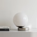 Modern Spherical White Table Lamp With Silver Base On White Tabletop