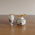 White Ceramic Vessels With Black Bamboo Patterns And Golden Leaf Lids On Wooden Tabletop