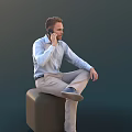 Man Talking On Phone Sitting On Black Cube With Light Blue Shirt And Beige Pants