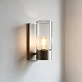 Modern Wall Sconce With Metal Frame Transparent Glass Shade And Illuminated Bulb On White Wall