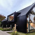 Modern Black Residential Building With Sloped Roof And Large Glass Windows Surrounded By Greenery