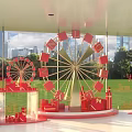 Decorative Ferris Wheel With Red Letters And Gift Boxes Against City Skyline And Green Grass