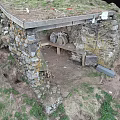Outdoor Stone Structure With Wooden Beam Bench And Dirt Ground Surrounded By Grass
