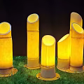 Bamboo Shaped Outdoor Lights Standing on Green Grass with Warm Yellow Glow in Night Scene