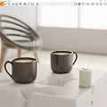 Steaming Black Mugs On White Table With Lit Candle In Bright Modern Room Setting