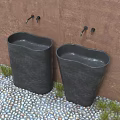 Two Black Freestanding Washbasins On Pebble Floor With Rusty Wall And Green Grass