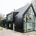 Modern Black Residential Building With Sloped Roof And Large Glass Windows Surrounded By Greenery