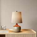 Beige Fabric Shade Table Lamp With Orange Neck Grayish Green Ceramic Base On Wooden Tray
