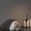 Gray Lazy Sofa With Blanket Next to Small Table Silver Sculptures Open Book Dark Floor