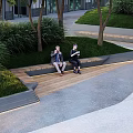 Modern Wooden Outdoor Bench In Urban Park With Greenery And People Sitting