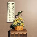 Wicker Basket Vase with Yellow Chrysanthemums and Green Leaves on Wooden Table with Calligraphy Scroll Background