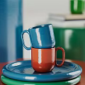 Vibrant Green Cup Beside Books With Blue Pitcher On Stacked Colorful Plates And Cylindrical Container