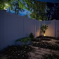 Serene Nighttime Outdoor Space With White Fence Stone Patio Green Plants And Striped Chair
