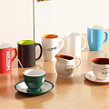Various Colored Ceramic Cups With Branded Text And Saucers On Wooden Table