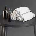White Rolled Bath Towels With Black Soap Dispensers And Small Flower Decor On Black Table
