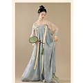 Woman in Traditional Light Blue Hanfu with Floral Patterns Holding Green Fan Against Beige Background