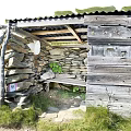 Traditional Stone And Wooden Hut Nestled In Grassy Natural Surroundings With Pathway And Greenery