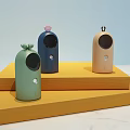 Three Different Colored Small Daily Electrical Appliances With Decorative Tops On Yellow Display Stands