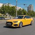 Yellow Audi Sedan Driving On City Street With Trees And Buildings