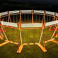Circular Outdoor Art Installation Featuring Orange Swings White Stripes Green Grass And Mountain Backdrop