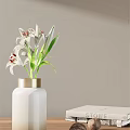 White Vase With Gold Rim Holding White Lilies Red Stamens And Green Leaves
