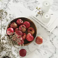 Fresh Red Apples in Wooden Bowl Alongside Books Candles and Dried Flowers on Marble Countertop