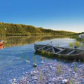 Peaceful Lake Scenery Featuring Red Brown Boats Pebble Shore Grass Green Woods And Blue Sky