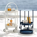 White And Blue Wheeled Two Tier Tea Trolley With Drinks Bottles Glasses In Outdoor Sunlight
