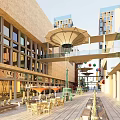 Vibrant Commercial Street With Modern Buildings Overhead Bridge Shaded Umbrellas And Outdoor Seating