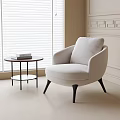 Beige Fabric Accent Chair With Black Legs By Window And Round Side Table With Books