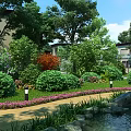 Serene Garden Landscape With Lush Trees Shrubs Pink Flowers Pathway Pond And Lamps