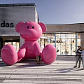 Large Pink Bear Sculpture Standing Outside Adidas Shopping Mall With Pedestrians