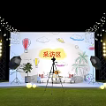 Interview Area Setup On Grass Floor With Hand Painted Backdrop String Lights And Camera Tripod