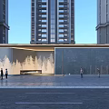 Modern Entrance Gate With Tree-Patterned Wall And Dark Stone Wall Near High-Rise Buildings With People Walking