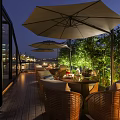 Restaurant Outdoor Terrace With Rattan Furniture Umbrellas Bamboo Plants And Night Harbor Lights
