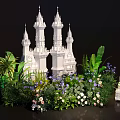 Lush Green Plant Wall Featuring Palm Leaves White Castle Model And Flowers With White Lanterns